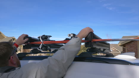 caucasian man loading a pair of snow skis into a ski rack, on top of a white vehicle