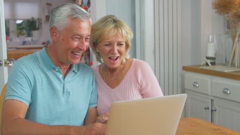 Pareja-De-Jubilados-Mayores-Sentados-Alrededor-De-Una-Mesa-En-Casa-Haciendo-Videollamadas-En-Una-Computadora-Portátil