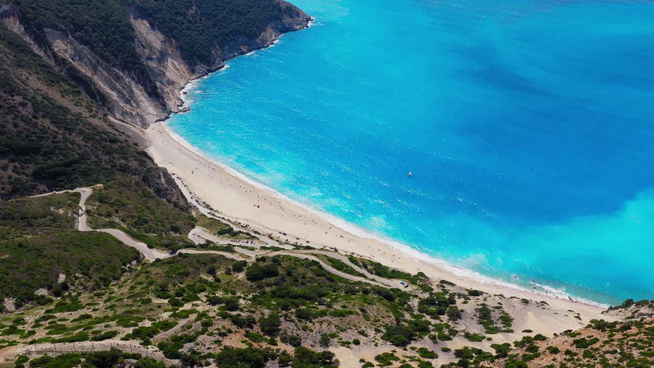 Drone panorama showing the sweeping arc of Myrtos Beach surrounded by rugged cliffs and blue Ionian waters