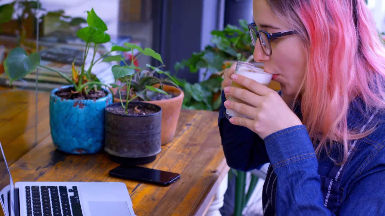 노트북 4k에서 일하는 동안 차가운 커피를 마시는 여성 소유자