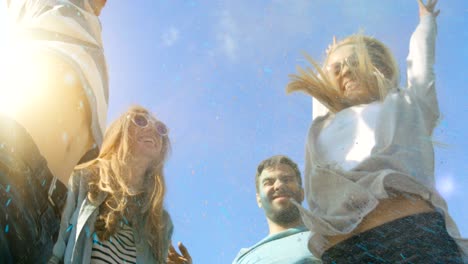 low angle shot of multi-ethnic group of diverse young people dancing and throwing colorful powder in the air in celebration of holi festival. they have enormous fun on this sunny day.