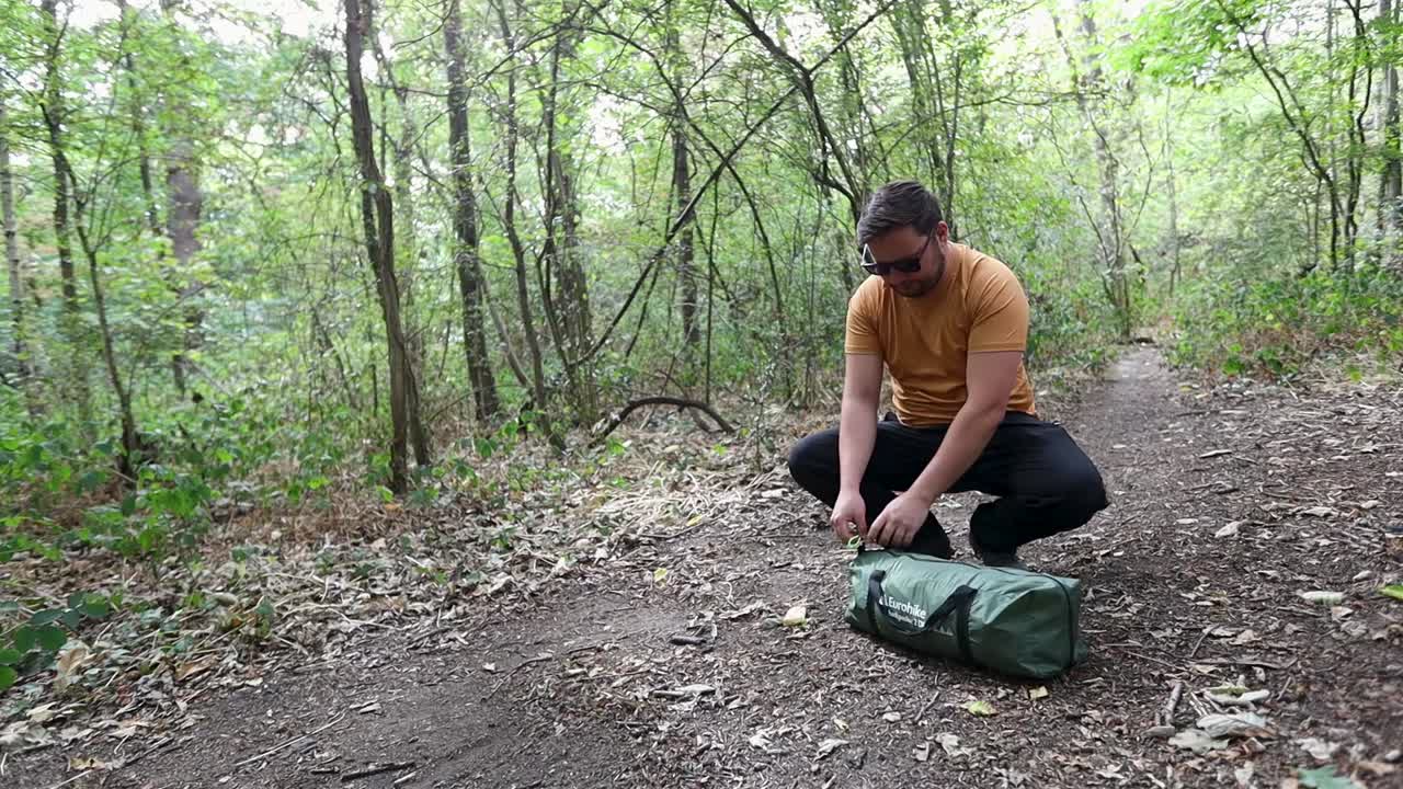 Man open bag and preparing tent for camping in forest, handheld view