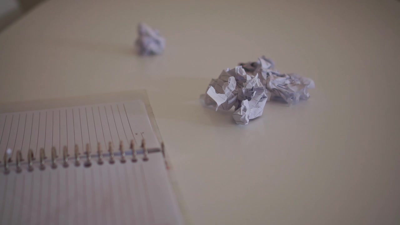 A hand throws a crumpled paper ball onto a desk beside a notebook, symbolizing frustration, failed ideas, productivity challenges, and the creative process.
