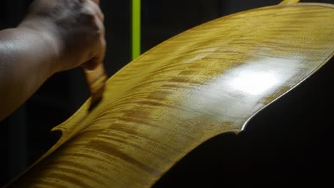 skilled luthier applying varnish on cello soundboard with spatula, showcasing meticulous woodworking technique within shadowy artisan workshop, real time