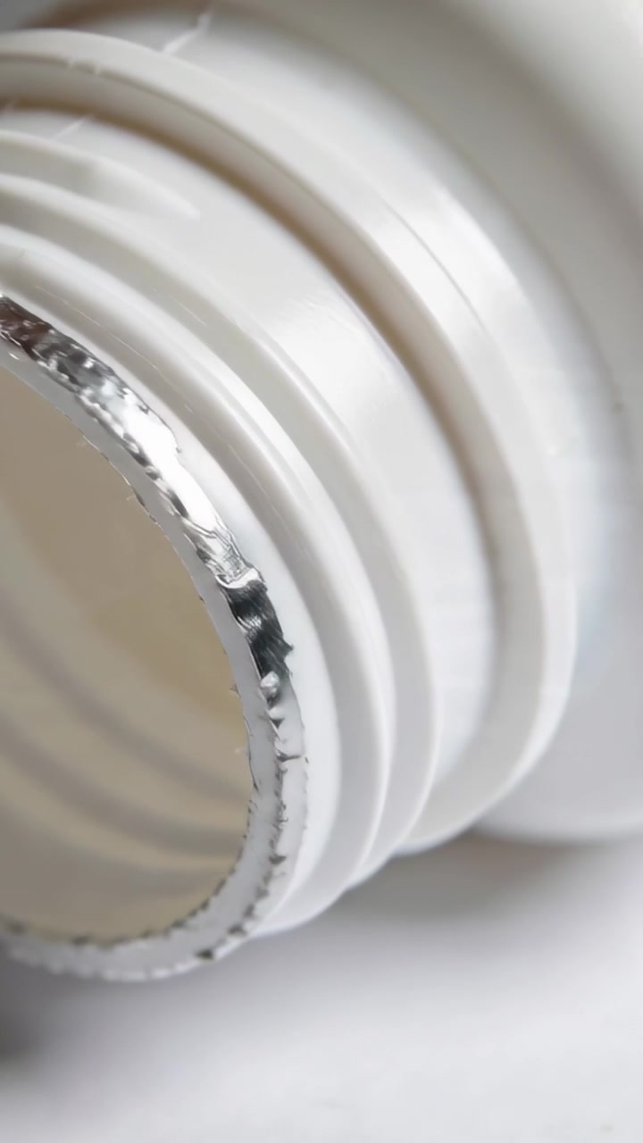 Vertical video: Panning camera inspecting white-plastic bottle neck on counter, showing foil chips