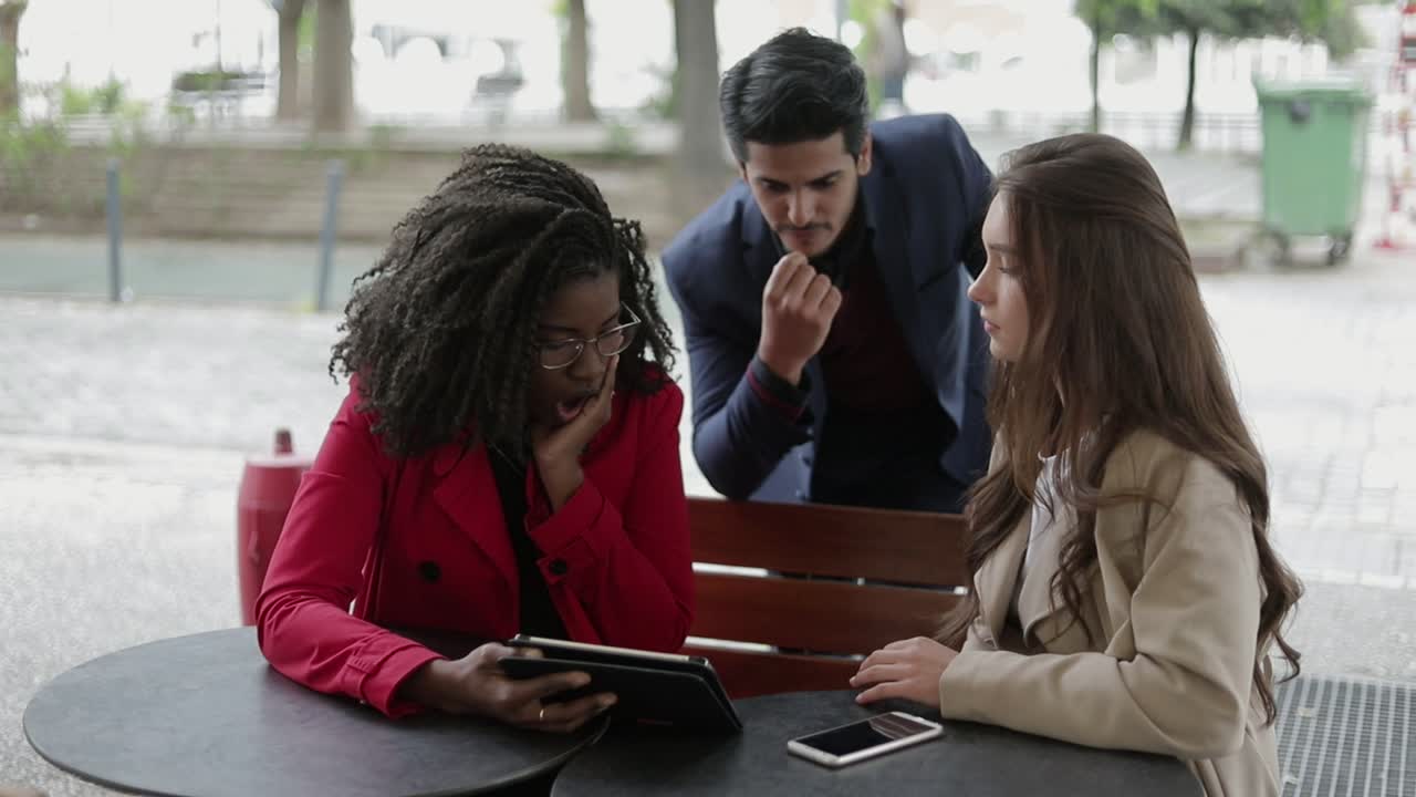 dos mujeres y un hombre en un café de verano mirando la tableta, discutiendo