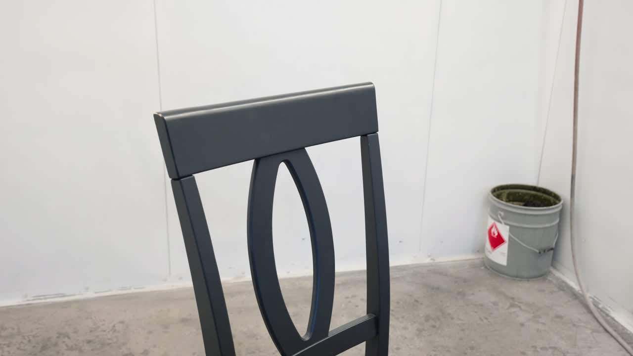 Camera rotates slowly around grey painted wooden chair back inside paint booth