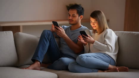 A couple relaxing on a couch while using their smartphones