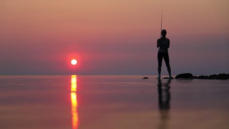 woman fishing on fishing rod spinning at sunset background.