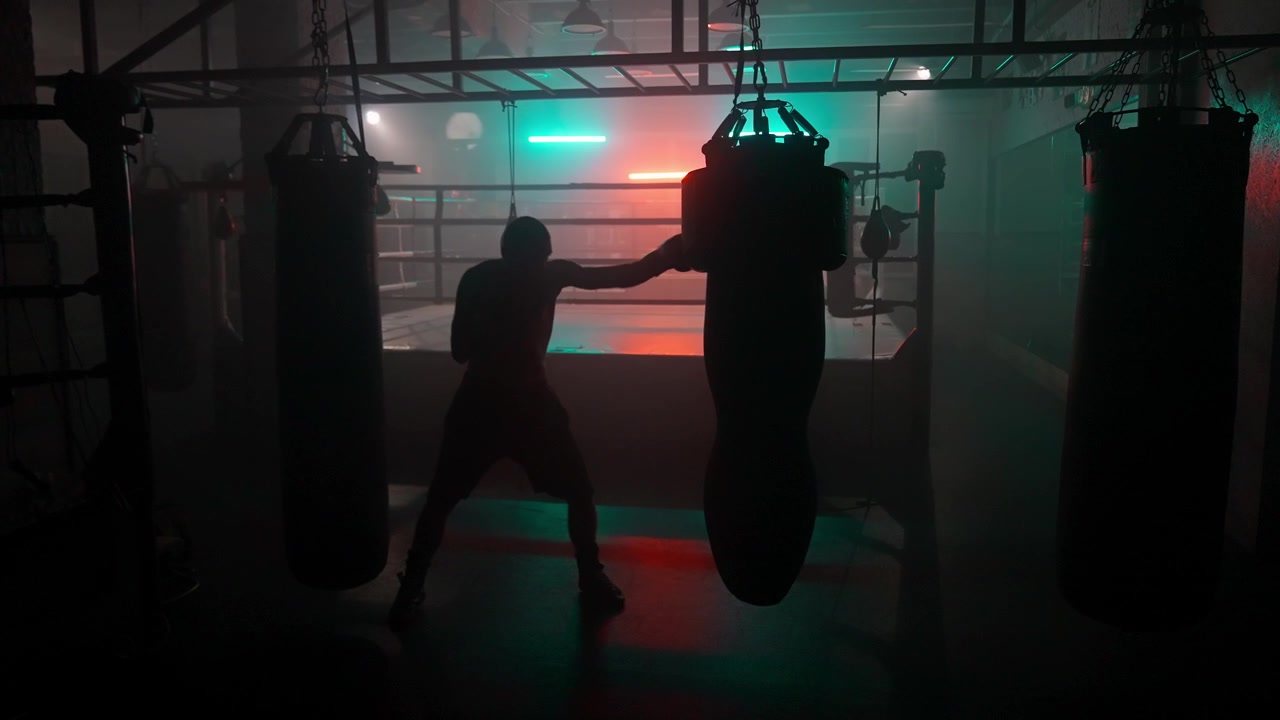Silhouette di un pugile che si allena con un sacco da boxe in una palestra buia con luci al neon