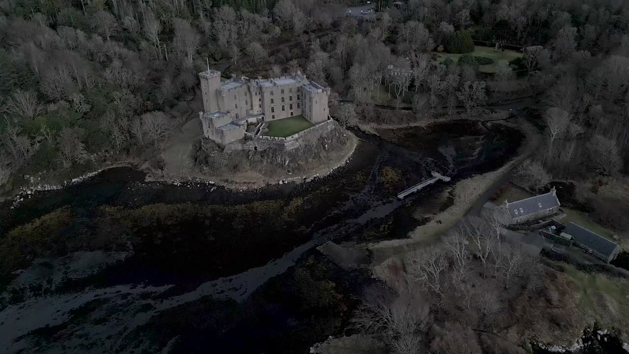 el castillo de dunvegan en la isla de skye, rodeado de bosques y agua, bajo un cielo nublado, vista aérea