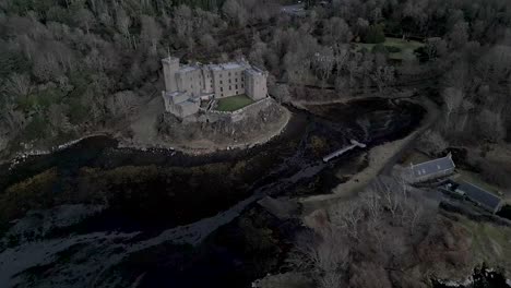 dunvegan castle on the isle of skye, surrounded by woodlands and water, under overcast skies, aerial view