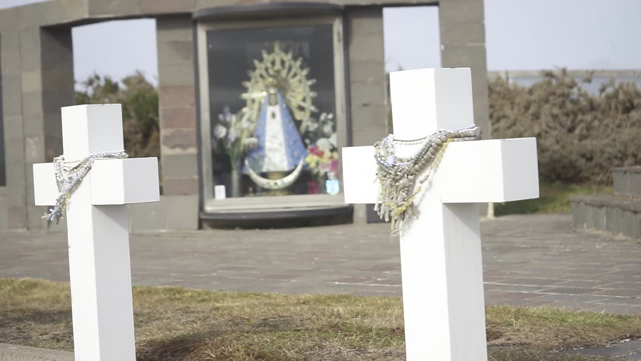 White crosses marking burial sites standing in somber cemetery grounds, with religious virgin mary statue watching over peaceful memorial landscape symbolizing spiritual remembrance