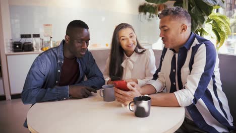 Cheerful-multiethnic-colleagues-browsing-smartphone-in-cafe