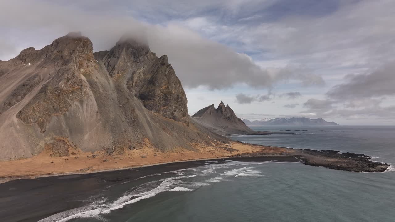 Vestrahorn, Eystrahorn and Brunnhorn peaks along Stokksnes coastline aerial view, stunning Icelandic landscape with black sands, ocean waves and skies.