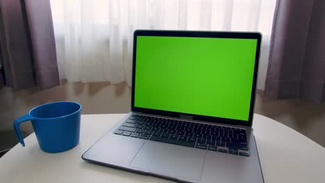 green screen (chroma key) laptop computer with blue plastic mug on white table