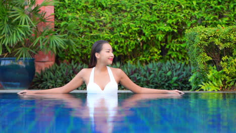 woman relaxing in swimming pool water leaning on the pool's edge in a tropical hotel lounge in indonesia, static slow-motion