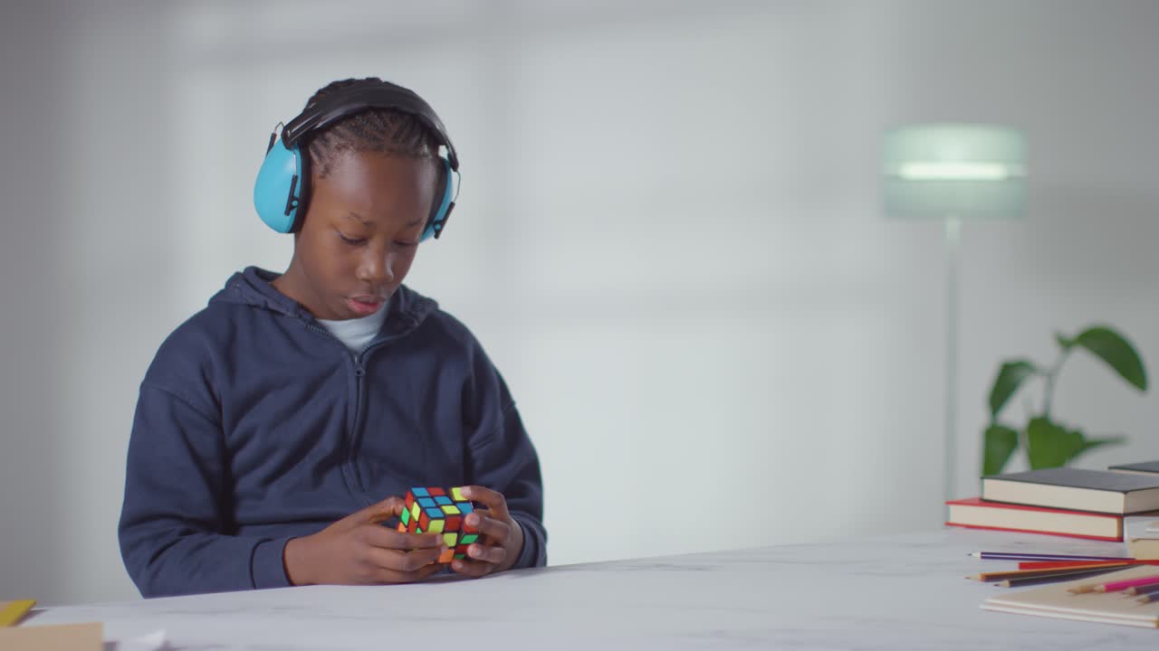 Boy On ASD Spectrum At Home Solving Puzzle Cube Wearing Ear Defenders 