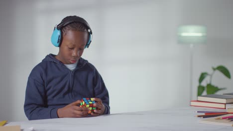 boy on asd spectrum at home solving puzzle cube wearing ear defenders