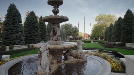 a crane stabilized shot of a beautiful and luxurious stone fountain framed by exquisite landscaping and rich nature tones