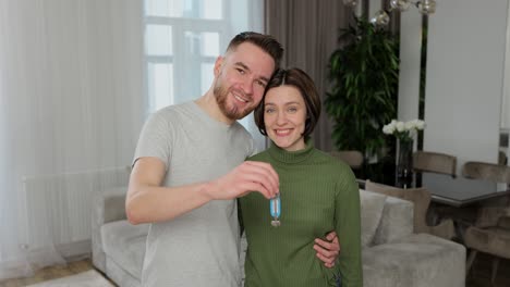 una joven pareja de familia feliz mirando a la cámara, mostrando las llaves de un nuevo apartamento. sintiéndose emocionados o comprando su propia casa o mudándose a un apartamento de alquiler. concepto de bienes raíces.
