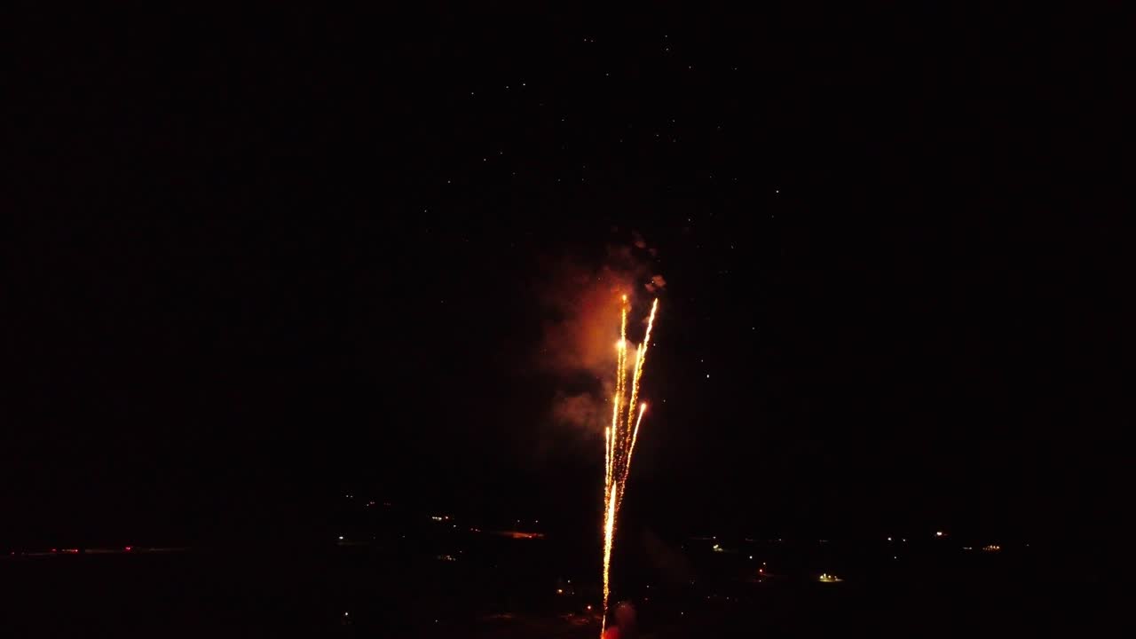 fuegos artificiales brillantes, vibrantes y coloridos finales que terminan explotando en la oscuridad mientras el dron vuela hacia atrás sobre el lago con reflejos en el agua, con la estrella fugaz final al final