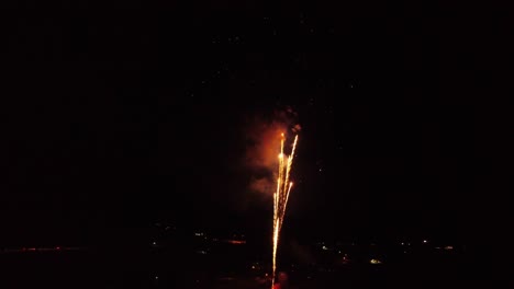 Feuerwerk,-Helles,-Lebendiges,-Farbenfrohes-Finale,-Das-Explodiert-Und-Im-Dunkeln-Losgeht,-Während-Die-Drohne-Rückwärts-über-Den-See-Fliegt,-Mit-Spiegelungen-Im-Wasser,-Mit-Der-Letzten-Sternschnuppe-Am-Ende