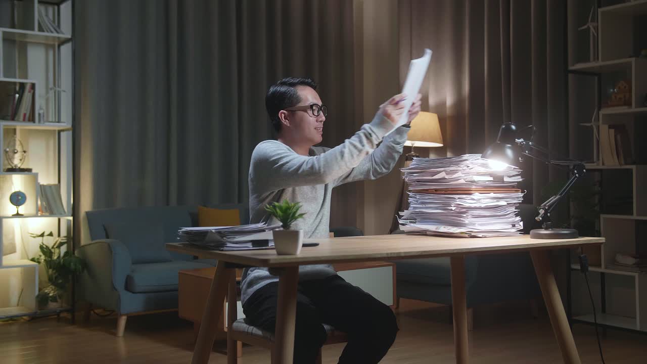 hombre asiático feliz celebrando el fin de trabajo con documentos en casa