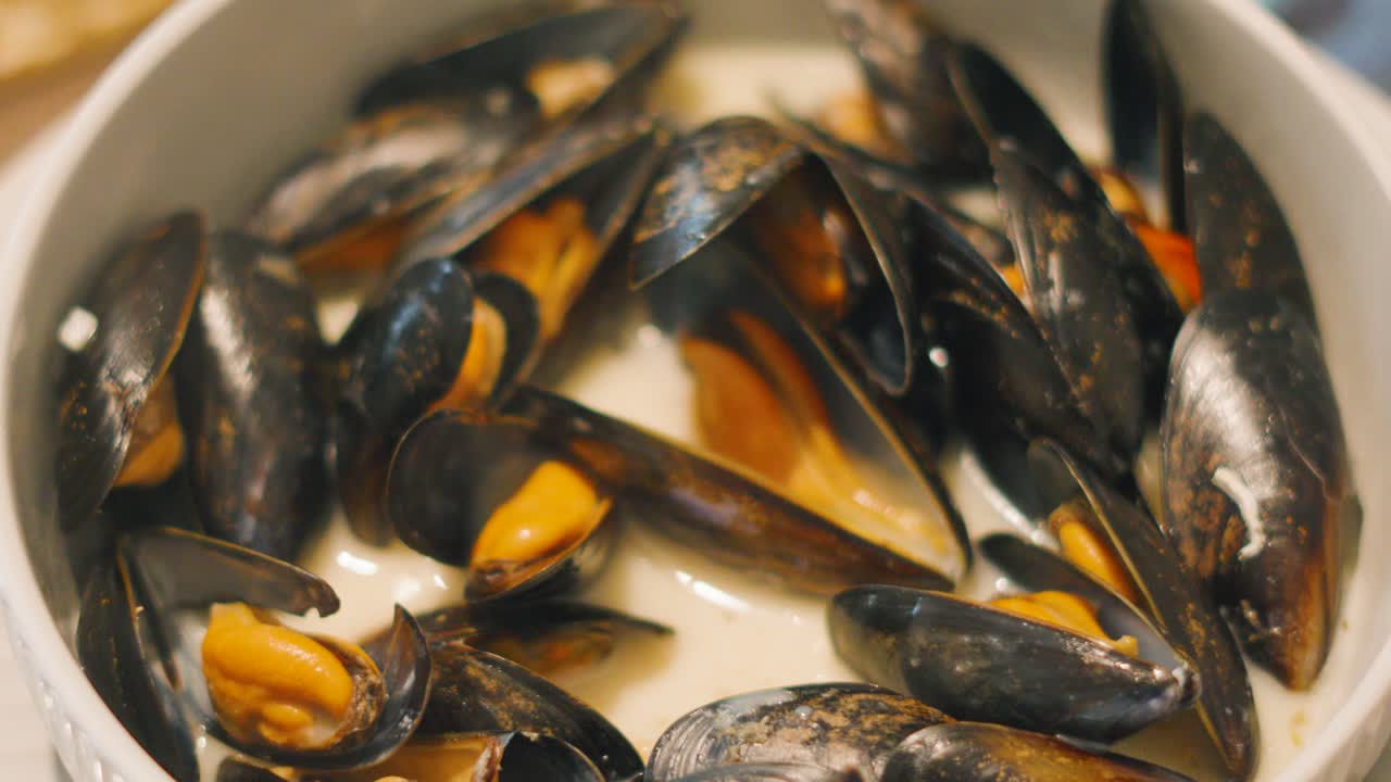 Top Overview of Mussels as Hand Reaches In and Takes Shellfish Out to Eat. Mollusks in White Wine Sauce