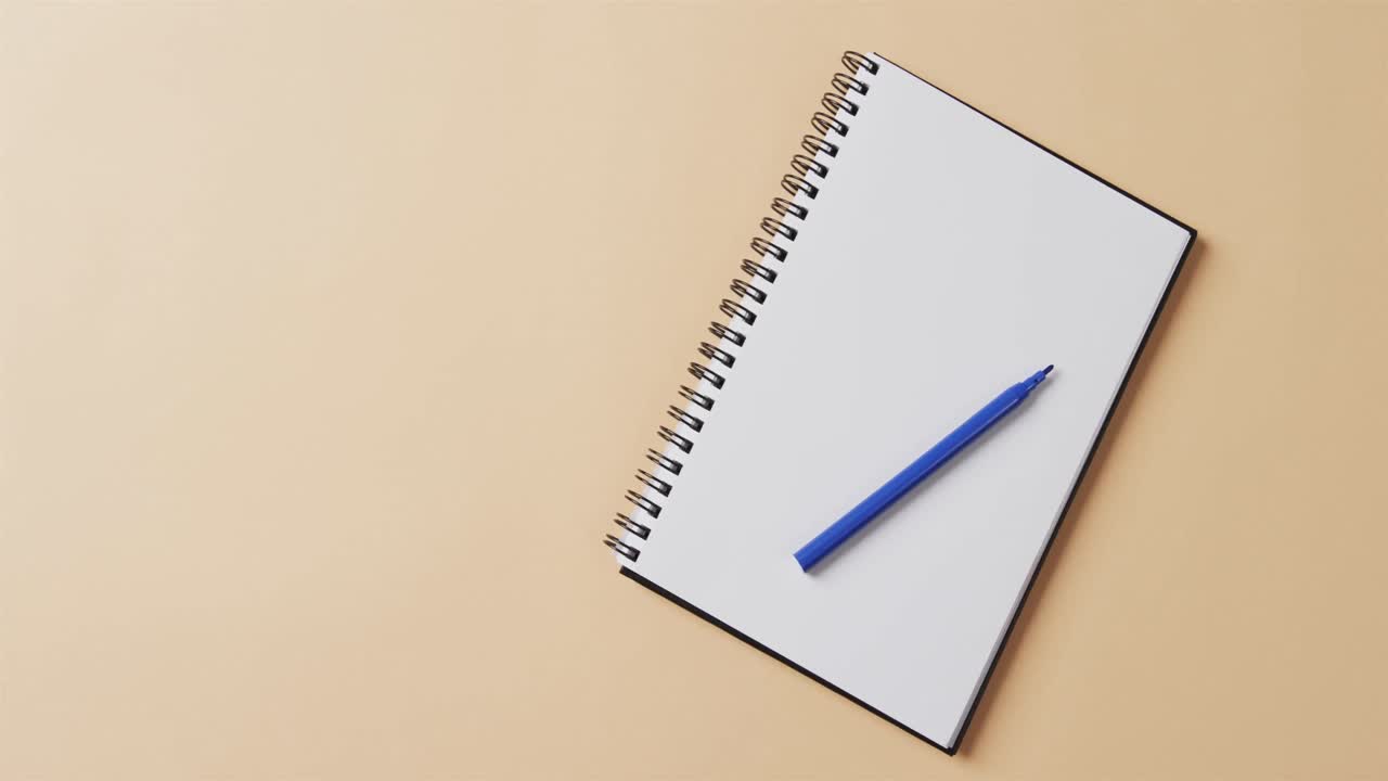 Overhead view of blue marker on notebook with copy space on beige background, in slow motion