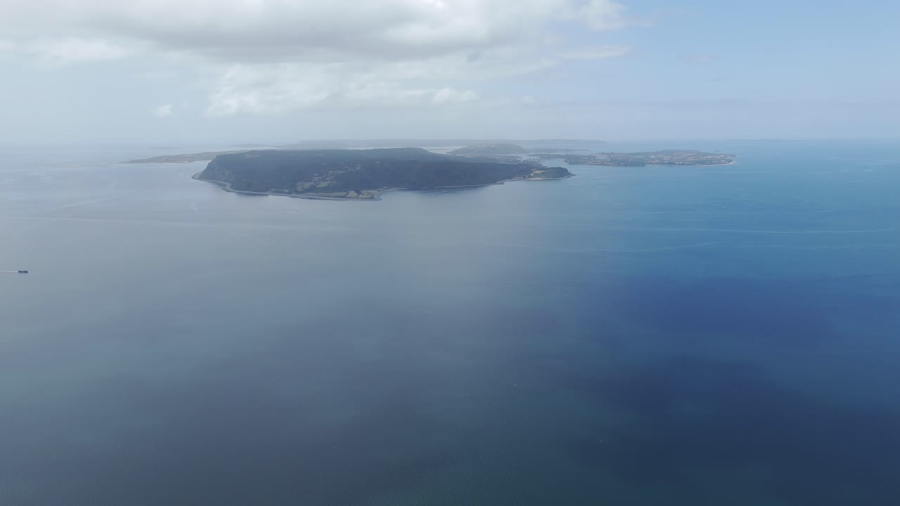 Aerial view showcasing the expansive coastline of Lemuy Island, surrounded by calm blue waters and under a partially cloudy sky
