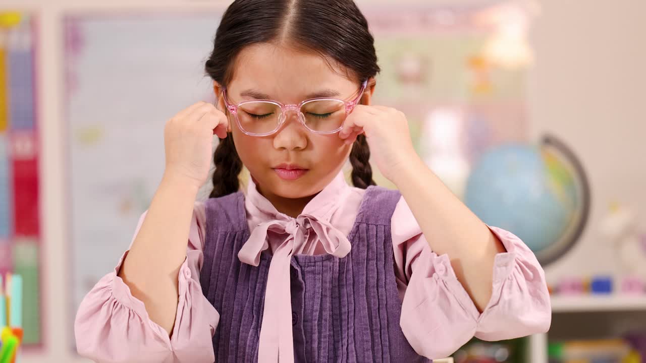 Ragazza con occhiali rosa che si massaggia le tempie e si concentra alla scrivania in una classe luminosa