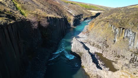 Aerial-drone-forward-moving-shot-over-rocky-cliff-along-studlagil-basalt-canyon,-Iceland-on-a-sunny-day