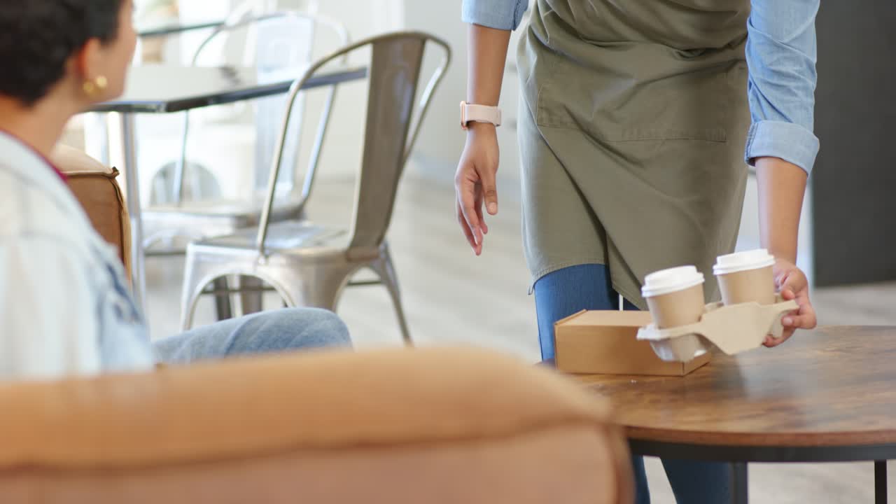 Kellnerin, die in einem Café hinter dem Tresen auftaucht und einem Kunden ein Kaffee-Tablett und eine Essensbox bringt