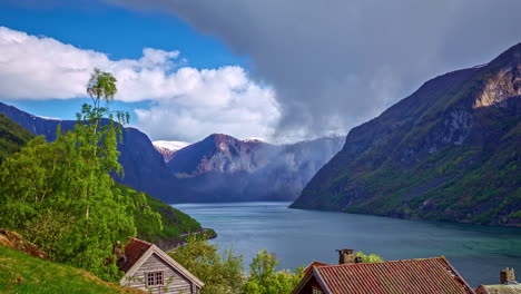 Landscape-with-picturesque-houses-between-mountains-and-a-lake-with-moving-clouds