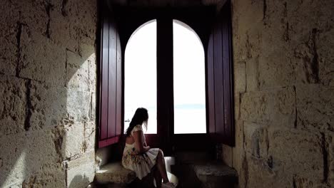 tourist woman sitting at a big window in belem tower in lisbon, portugal - pullback