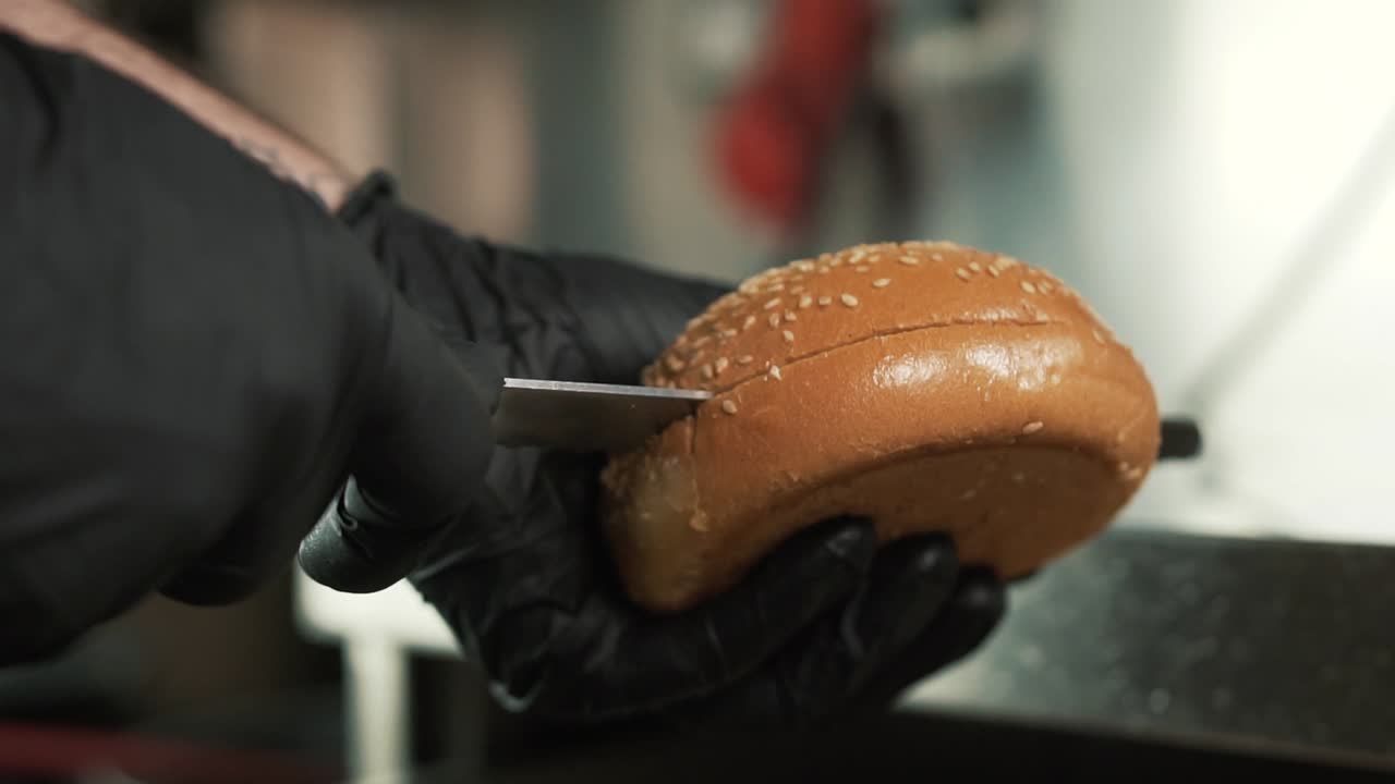 Hands with black gloves cut burger bread in two slices. Slow-motion