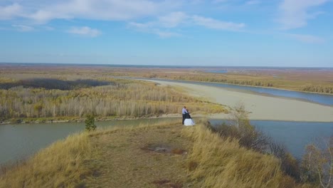 newly-wedded-couple-hugs-on-steep-bank-near-river-upper-view