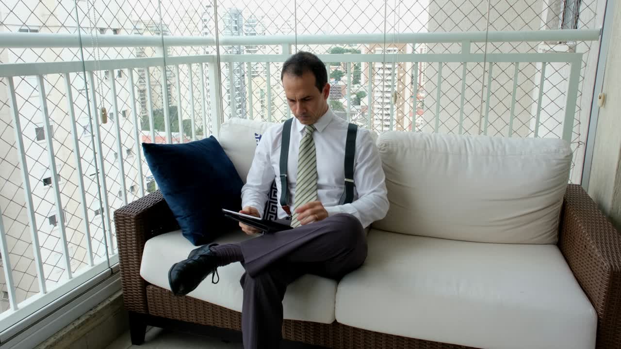 타이와 서펜서를 입은 남자가 태블릿을 가지고 일하며 불쾌한 표정과 몸짓을 하고 있습니다.