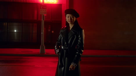 young woman in a leather coat and beret under red neon light at night