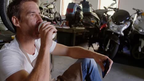 mecánico masculino bebiendo café en el garaje de reparación de motocicletas 4k