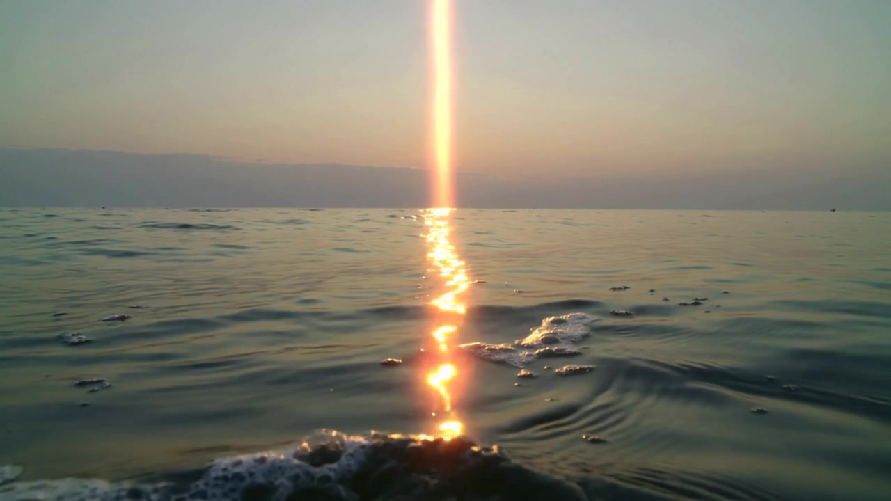 海の低い太陽に照らされ、きらめく中央の太陽の反射光の道と水面、泡を伴う。