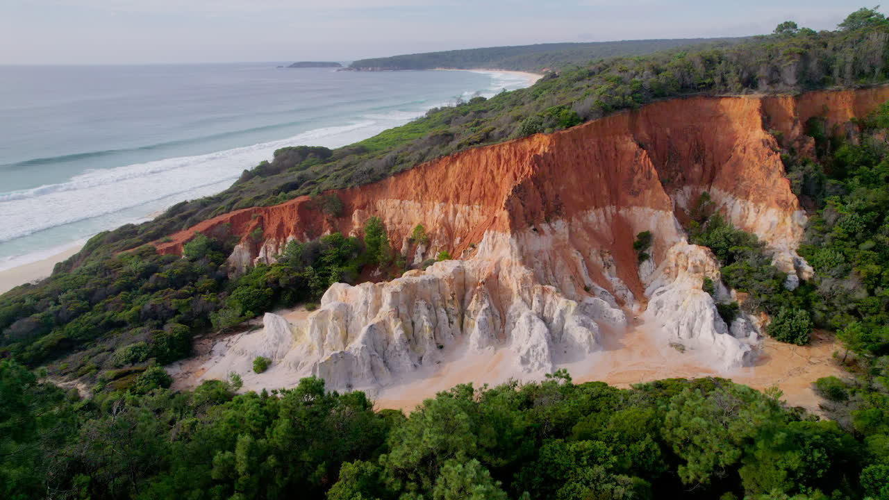 Scenic drone flight over The Pinnacles in Beowa National Park, revealing colorful cliffs and surfable waves in the distance. Aerial footage capturing nature's beauty along the wild NSW coastline