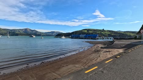 a serene drive along akaroa's waterfront, capturing calm waters, boats, and vibrant sunrise hues in a tranquil setting