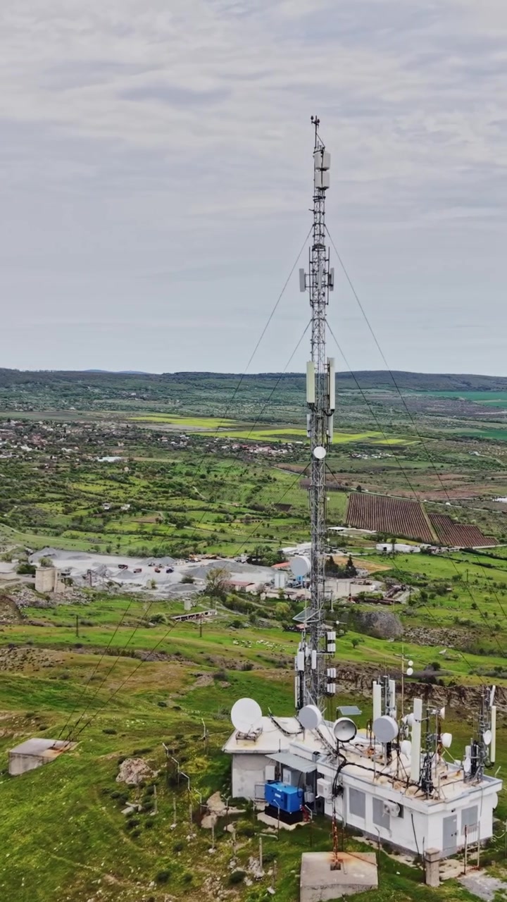 Una torre di comunicazione si erge su una collina che domina campi verdi in primavera.