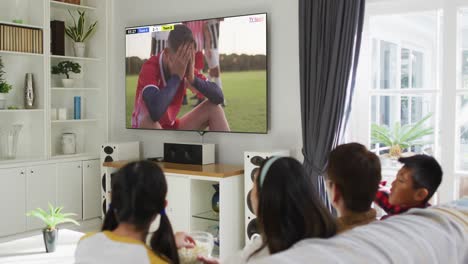 Video-Eines-Asiatischen-Paares-Mit-Sohn-Und-Tochter,-Die-Auf-Dem-Sofa-Sitzen-Und-Zu-Hause-Fußball-Schauen