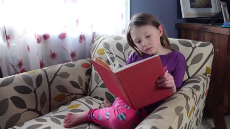 niña sentada en una silla leyendo un libro en un hermoso día cálido y soleado y acogedor mientras feliz - tiro medio