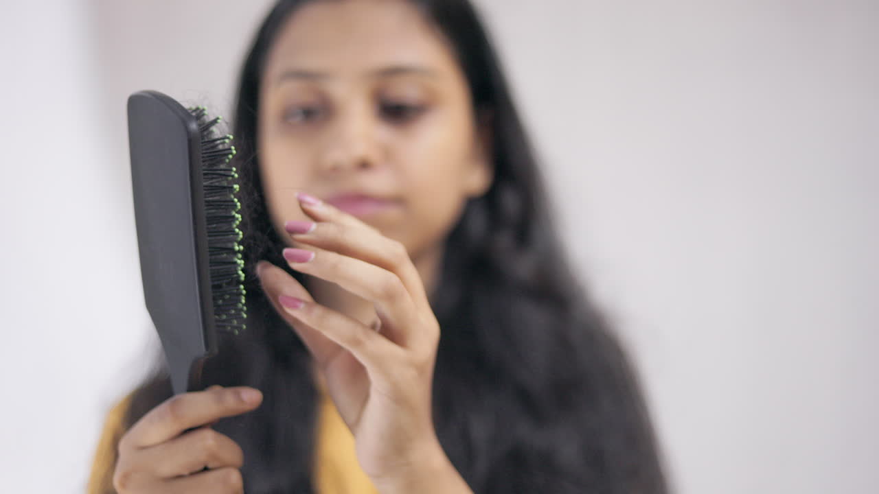 young woman shocked and worried after removing lost hair from the comb, focus on comb, hair care concept.