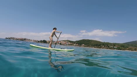 bikini woman stand up surfboard rowing in sithonia, greece, tracking