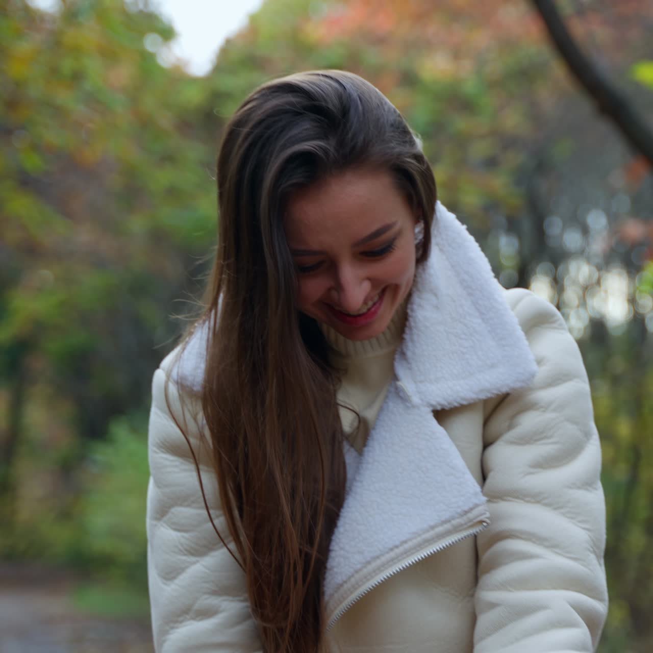 Happy lady with long dark hair taking selfie on her phone. Young positive woman changing positions to take the best pictures. Autumn nature in blur at backdrop